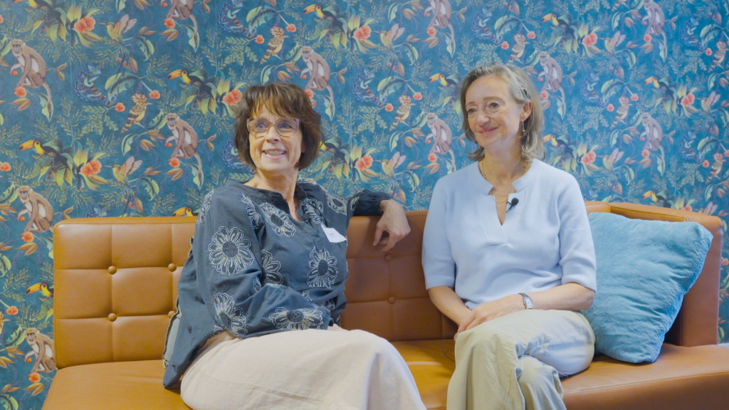 Twee vrouwen zitten naast ekaar op een bank en kijken lachend
