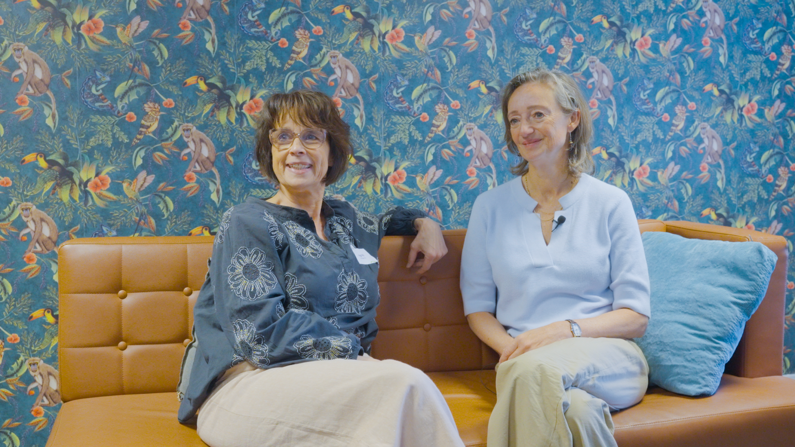 Twee vrouwen zitten naast ekaar op een bank en kijken lachend